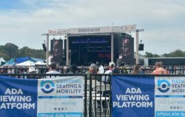 View from a wheelchair-accessible platform looking toward a stage, outdoors and under blue skies with clouds.