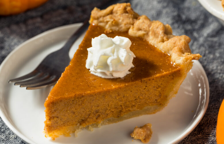 Slice of pumpkin pie with whipped cream on a round white plate.