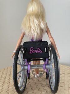 The view from the back of Barbie's wheelchair show Barbie's arms out straight toward the wheels.