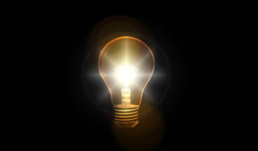 Lit light bulb against a black background.