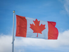 Canadian flag flies against blue sky with white clouds.