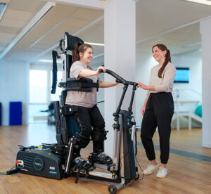 A mobility client uses the Innowalk with the help of a clinician. They are in a clinic or therapy room.