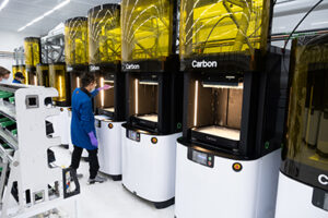 A technician wearing blue stands before one of four Carbon 3D printers.