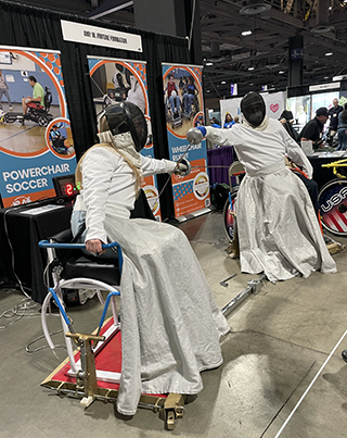 Two wheelchair fencers duel while in full gear.