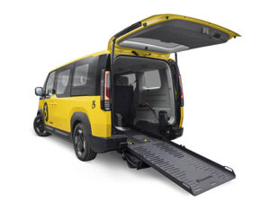 A yellow taxi-styled Kia PV5 WAV is shown from the back with the ramp deployed.
