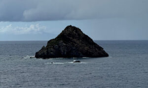 Rocky, steep small island in the middle of a blue-gray sea.