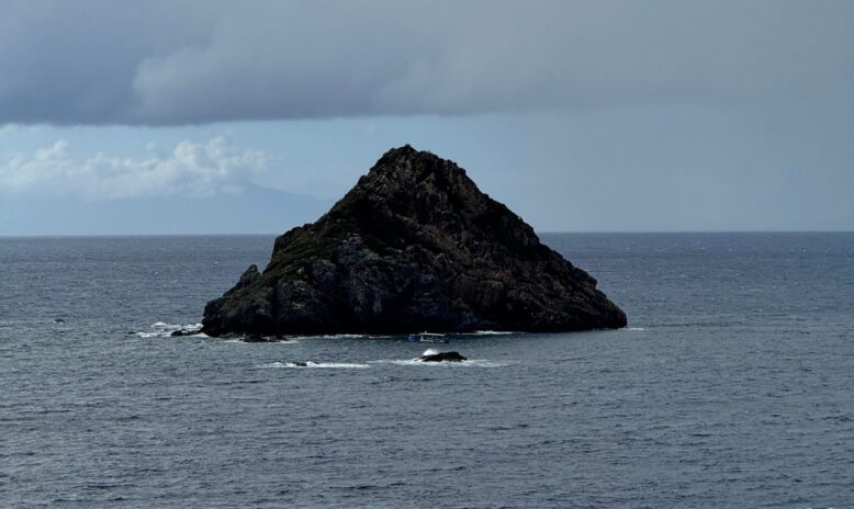 Rocky, steep small island in the middle of a blue-gray sea.